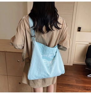 Detail of light blue canvas tote bag showing bow print and adjustable shoulder strap on model