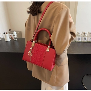 Red bridal shoulder bag featuring a woven handle and heart-shaped charm with wedding detail