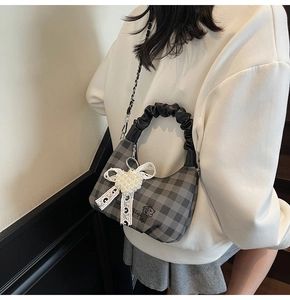 Detail of grey plaid hobo bag with pearl heart bow and chain strap on model