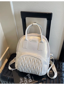 Minimalist white pleated backpack with pearl luster finish on a black suitcase handle