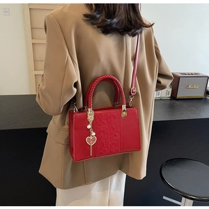 Detail of red bridal handbag with woven handle and heart-shaped pearl pendant charm