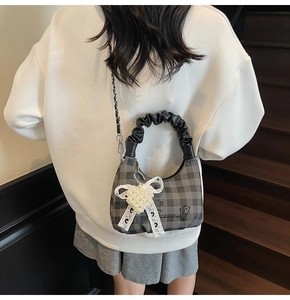Detail of checkered crossbody bag with pearl heart charm and ruffled leather handle