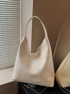 Minimalist beige woven tote bag with premium leather texture on a stack of books