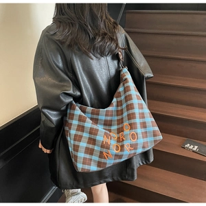Détail du sac fourre-tout en toile à carreaux bleu et marron avec broderie orange sur l'épaule