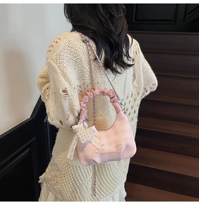 Pink checkered dumpling bag with pearl heart charm on model standing on wooden stairs