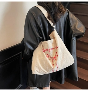 Close-up of adjustable strap and red ribbon print on a cream canvas tote bag