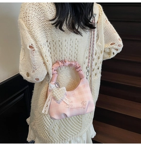 Detail of pink plaid bag with lace heart charm and embroidery on a knit sweater