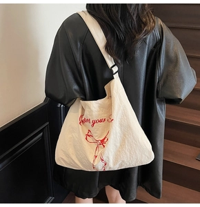 Detail of a large cream canvas tote with red bow print and adjustable black shoulder strap