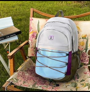 Détail d'un sac à dos coloré avec écusson floral et sandow posé sur une chaise pliante