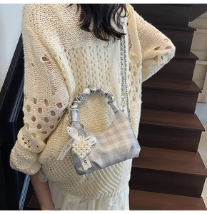 Close-up of silver plaid dumpling bag with pearl heart charm and metal chain strap