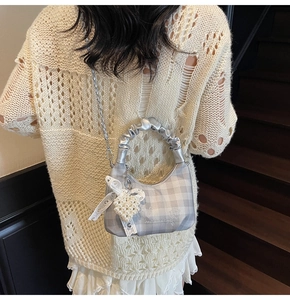 Detail of grey checkered crossbody bag with silver chain, lace bow and pearl heart charm