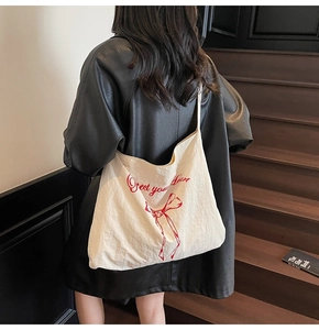 Detail of canvas tote bag featuring red Direct your Heart text and bow on model