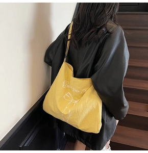 Detail of yellow canvas tote bag with bow print worn by model on black jacket