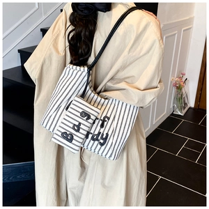 Detail of a black and white striped tote bag with letter patch worn with a beige trench coat