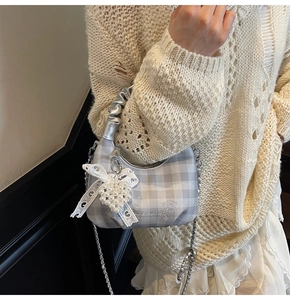 Close-up of plaid bag with silver chain, pearl heart charm, and lace bow detail