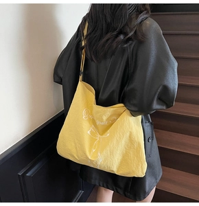 Close-up of yellow large canvas tote bag with white bow print worn over black leather jacket