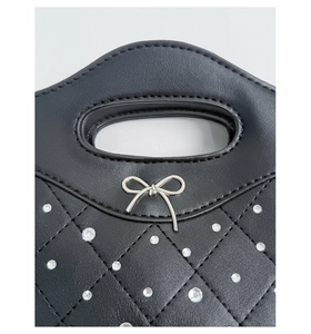 Detail of black quilted leather handbag with rhinestones and metal bow accent