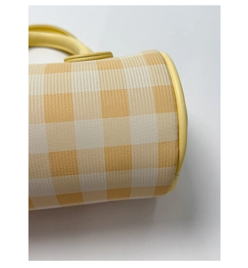 Détail du sac cylindrique à carreaux jaunes et blancs avec bordure et poignée en cuir