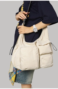 Detail of a large off-white nylon messenger bag with multiple utility pockets and drawstring