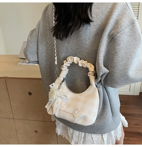 Close-up of cream checkered crossbody bag with pearl bow charm and cloud handle