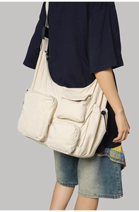 Side view of a large cream messenger bag with multi-pocket details and adjustable strap