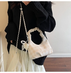 Detailed close-up of beige plaid hobo bag with pearl heart charm and ruffled handle