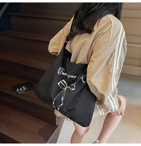 Detail of a large black canvas tote bag featuring a white bow print and cursive art text