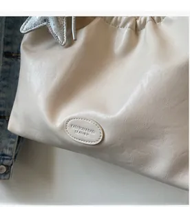 Close-up of cream leather tote bag featuring a silver star charm and embossed fashion label