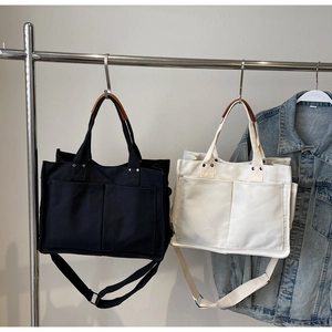 Detail of canvas tote bags featuring front pockets, leather handles and adjustable straps