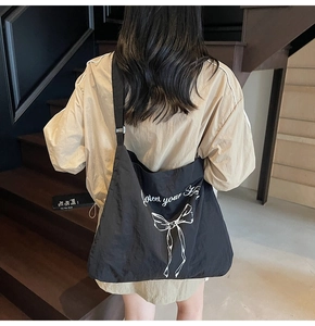 Detail of a black large-capacity tote bag with adjustable strap and white bow print