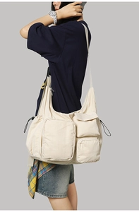 Detailed side view of a large cream messenger bag with multi-pockets on a model