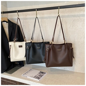 Dettaglio delle borse tote in pelle beige, nera e marrone appese a un supporto di metallo