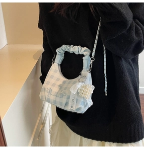 Detail of blue and white checkered crossbody bag with pearl heart charm on a model
