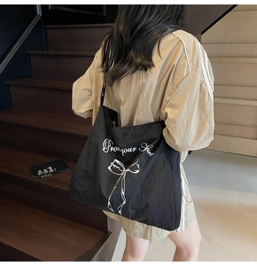 Detail of large black nylon tote bag featuring white bow print and stylish lettering