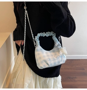 Detail of light blue checkered handbag with ruffle handle and pearl bow pendant