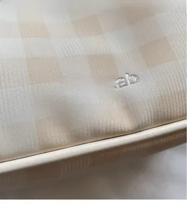 Detailed macro view of the silver branded logo on cream plaid canvas crossbody bag