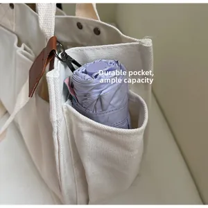 Detail of a white canvas tote bag side pocket holding a purple folding umbrella
