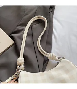 Detail of cream checkered handbag featuring a stylish knotted handle and silk scarf decor