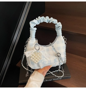 Detail of blue checkerboard bag featuring pearl heart charm and ruffled top handle