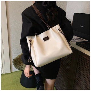 Dettaglio della grande borsa tote bianca con manici marroni e targhetta in metallo