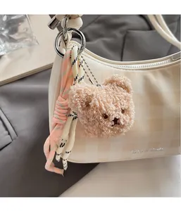 Close-up of a plush bear charm on a plaid crescent bag with woven pink and black lanyards