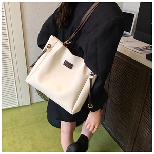 Dettaglio di una grande borsa tote crema con cinturini marroni e logo in metallo
