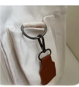 Detail of gunmetal hardware with brown leather trim on a white canvas tote bag