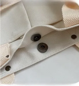 Detail view of the strong magnetic snap closure on a cream canvas tote bag