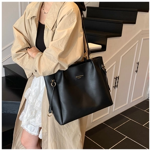 Dettaglio di una grande borsa tote nera minimalista indossata a spalla da una modella
