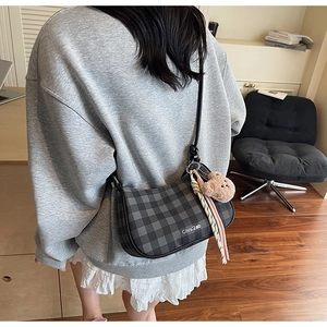 Detail of checkered underarm bag with cute brown bear plush charm and woven strap