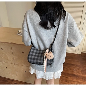 Detail of checkered hobo bag with teddy bear charm and silver brand logo on crossbody strap