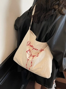 Large cream canvas tote bag with red bow print shown on a model in a black leather coat