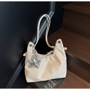 Détail du sac à bandoulière plissé crème avec breloque étoile sur escalier sombre