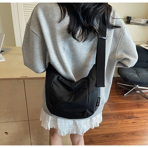 Detail of a black nylon crossbody bag with adjustable strap and logo tag shown on a model